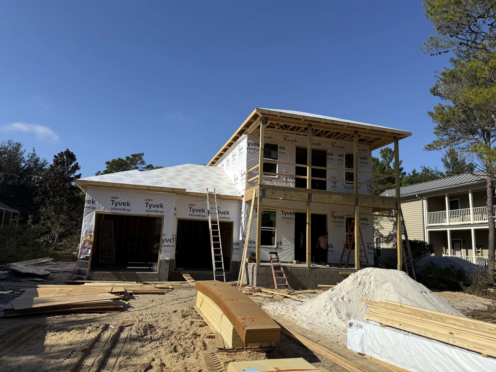 New construction two-story house, framed and wrapped, with a garage and front porch structure, materials on site.